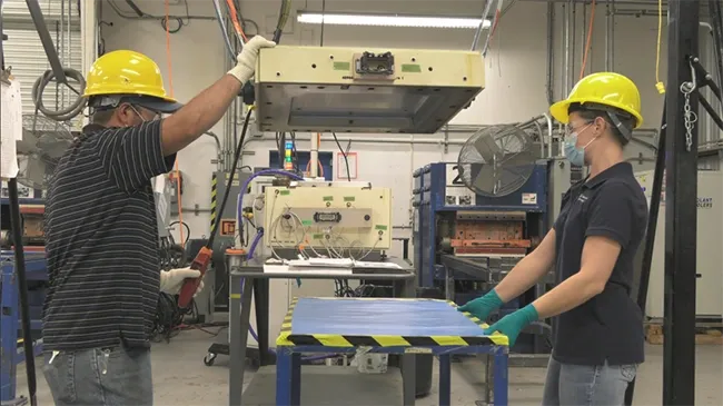 Two people in a factory with one holding onto the arm of another person.